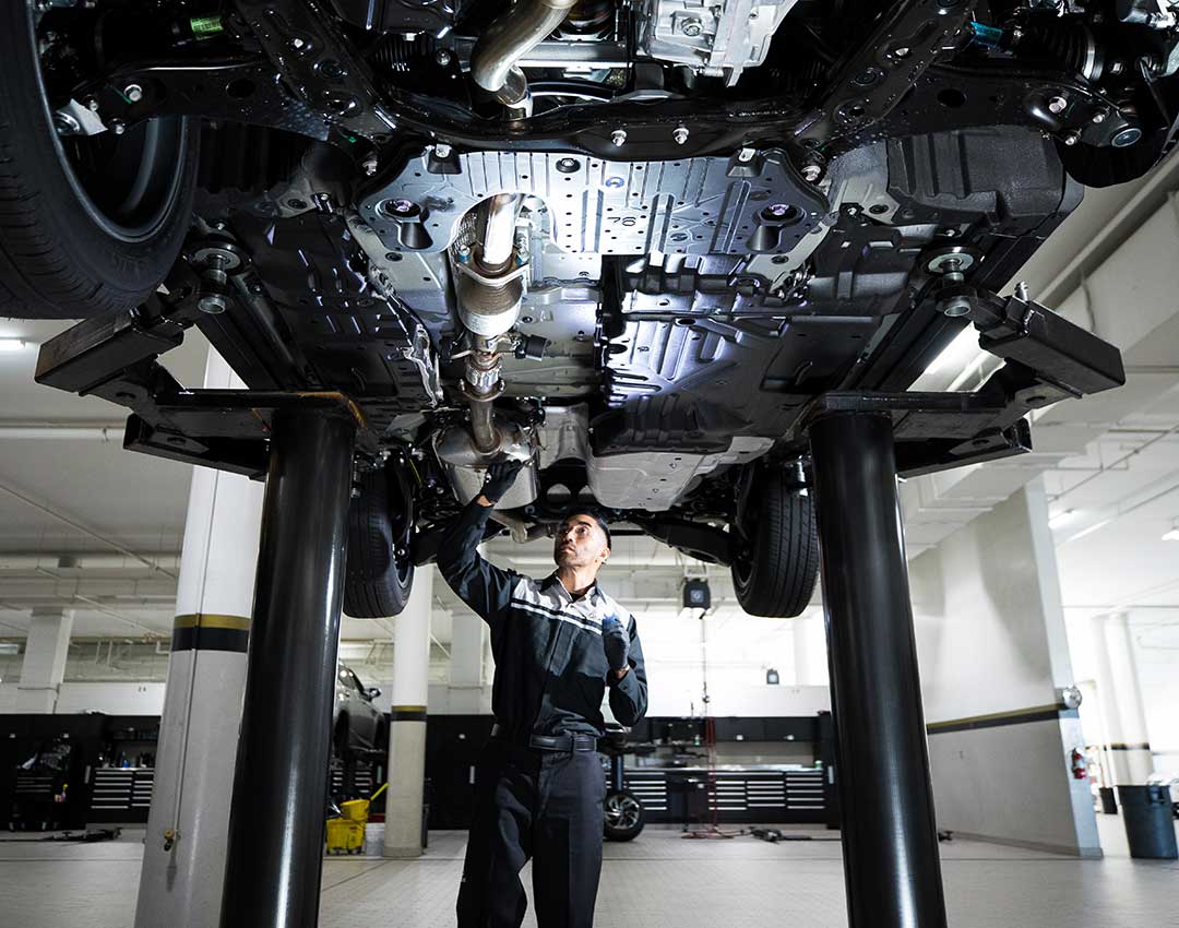 Lexus service mechanic standing under a car on a hoist