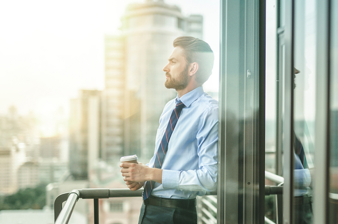 Man stands on an office balcony with a coffee cup in his hand.
