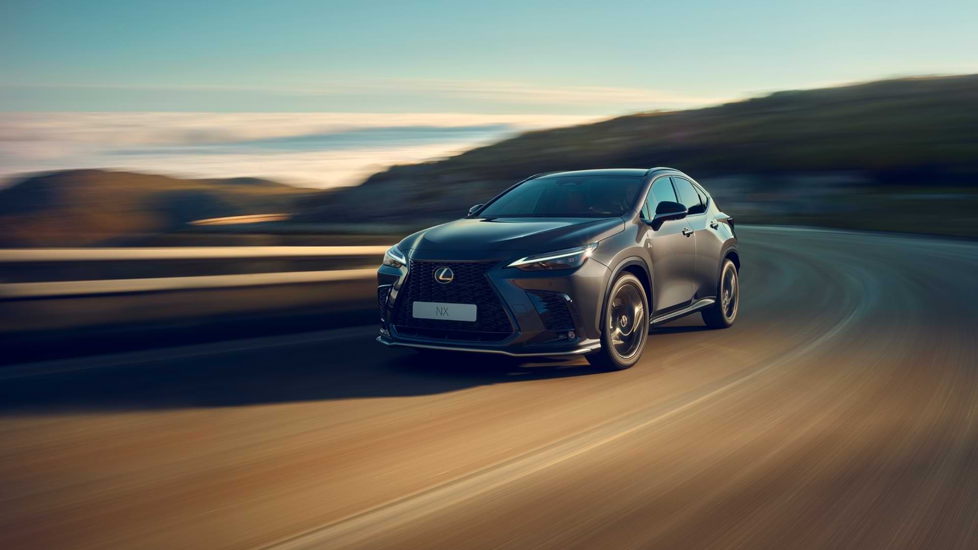 A dark grey 2022 Lexus NX drives across a baron highway. The surroundings are blurred, as if the NX speeds along.