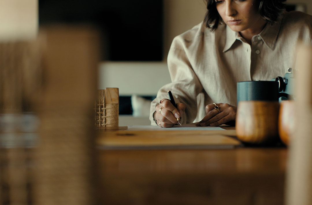 A woman in a shirt writes on a wooden desk.